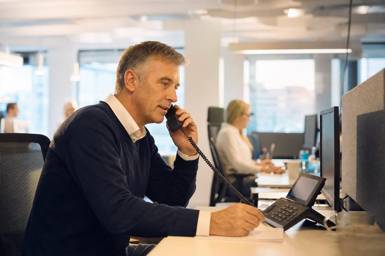 Recruiter im Büro am Telefon, daneben Notizblock und Tischapparat